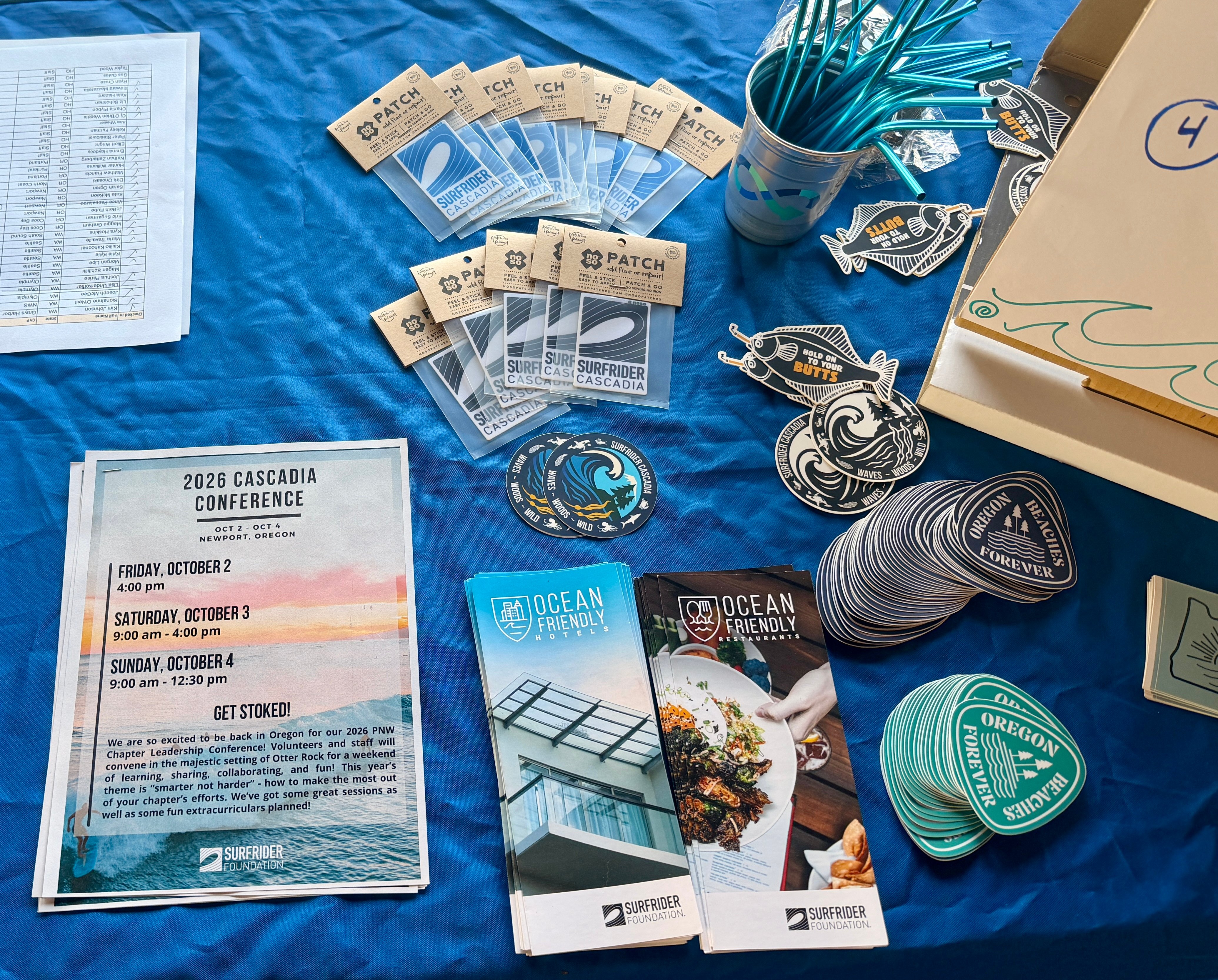 Stickers, agenda, flyers, and metal straws displayed on a table with a blue tablecloth