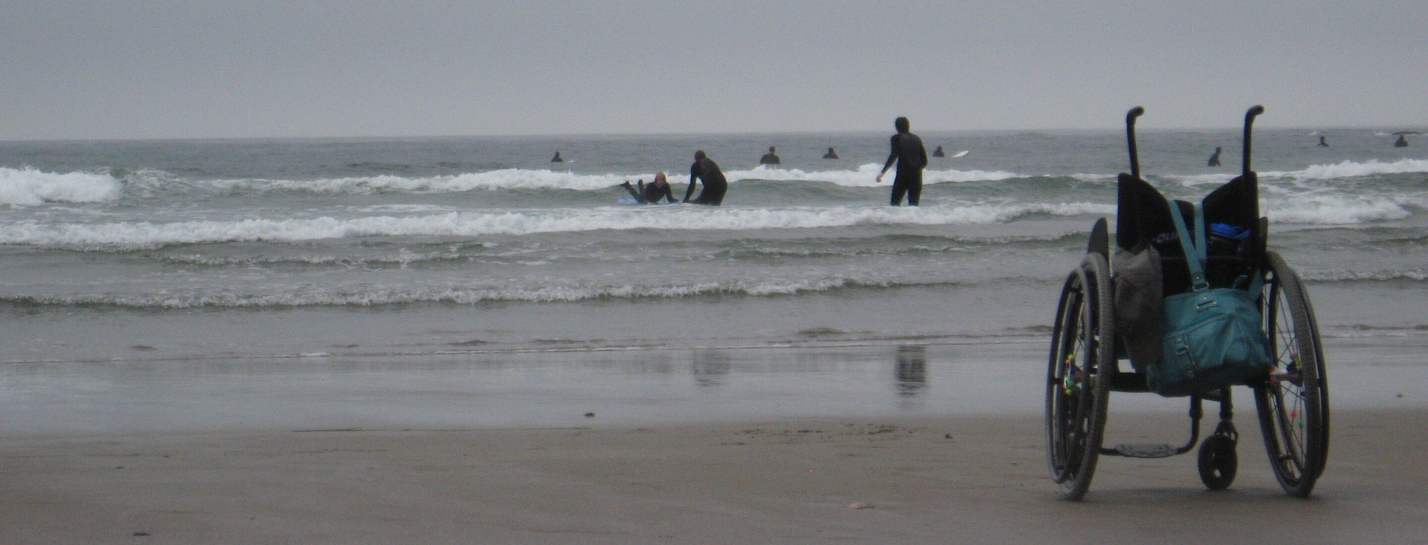 photo of beach and surfers with wheelchair in foreground